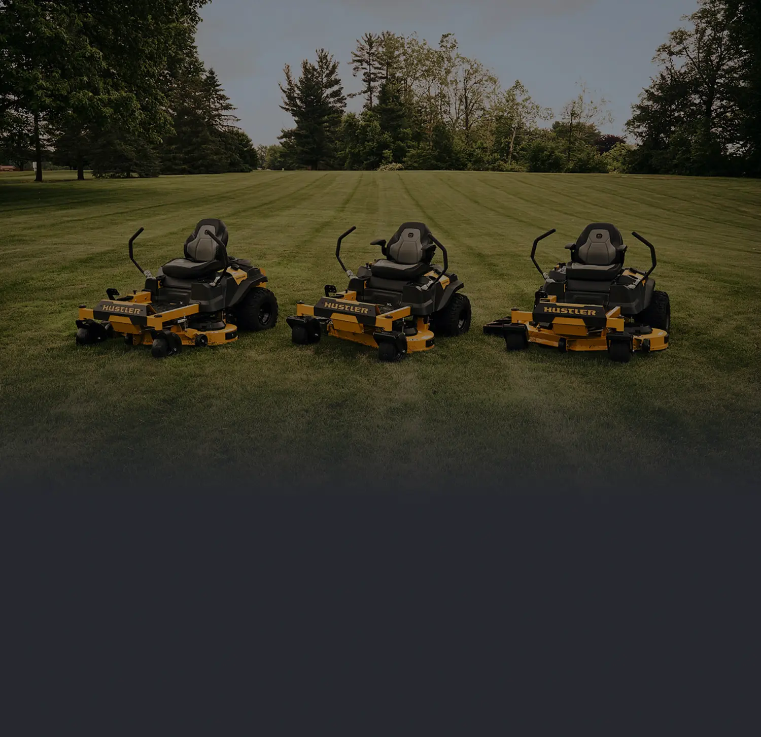 hero_img Three yellow-and-black Hustler zero-turn lawn mowers lined up on a grassy field with trees in the background.
